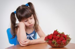 Girl sadly looks at the plate with strawberries
