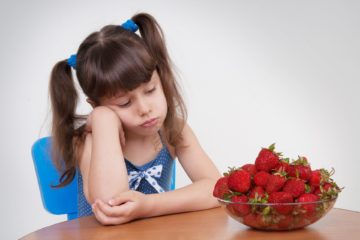Girl sadly looks at the plate with strawberries