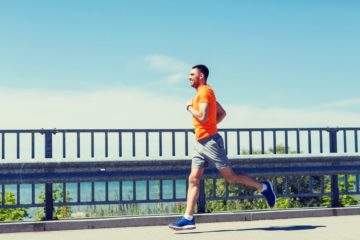 Smiling young man with heart rate watch running at summer seaside