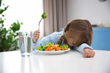 girl with head on table and fork of broccoli